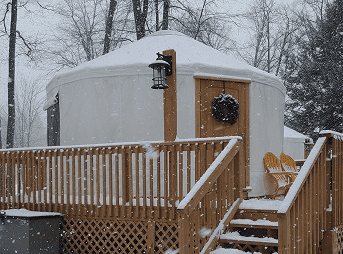 Yurt surrounded by snow in a winter forest setting, perfect for cozy yurt stays.
