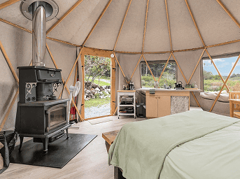Yurt interior featuring a wood stove, large windows, and comfortable bedding for a unique glamping e.