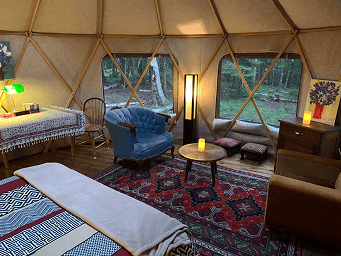 Yurt interior featuring comfortable seating, colorful rugs, and large windows with scenic views. Per.