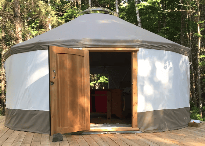 Yurt with open wooden door in forest setting for outdoor accommodation.
