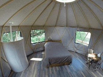 Interior view of a cozy yurt with wooden floors and large windows, perfect for a memorable yurt stay.