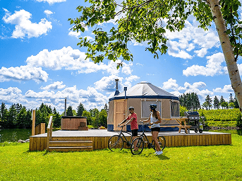 Cozy yurt surrounded by lush greenery and blue sky, ideal for outdoor glamping experiences.