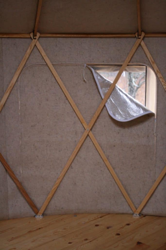 Yurta interior wall featuring a small window and wooden lattice structure.