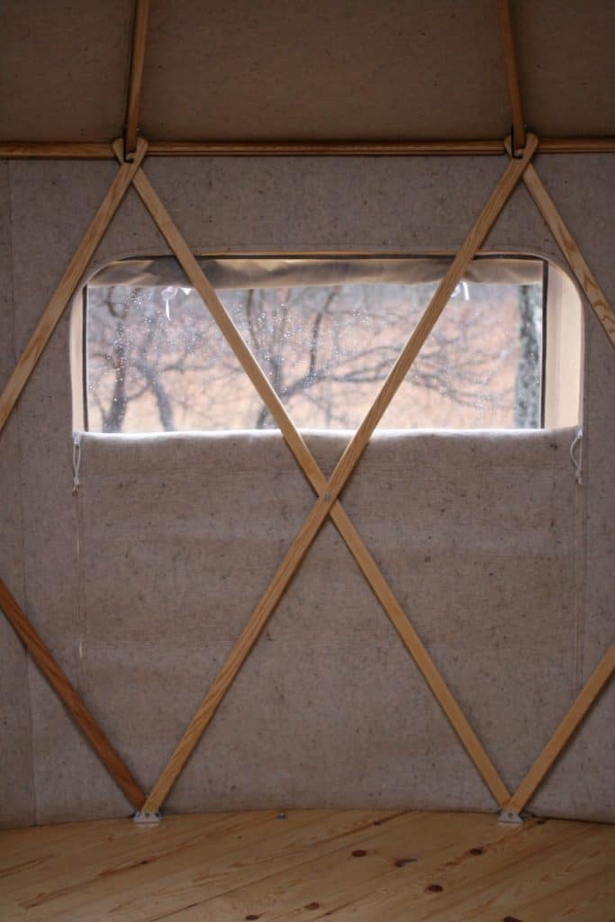 Yurta interior with window and wooden support beams, showcasing traditional design and craftsmanship.