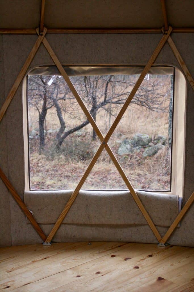 Yurta interior with large window overlooking trees and nature scene.